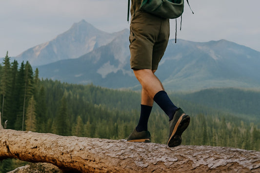 Close-up of a hiker balancing on a log with mountains behind—banner for Laetts multifunctional socks combining HygroHeat™ FIR warmth, BootGlide™ low-friction fit, Merino moisture control, and optional compression for versatile outdoor use.