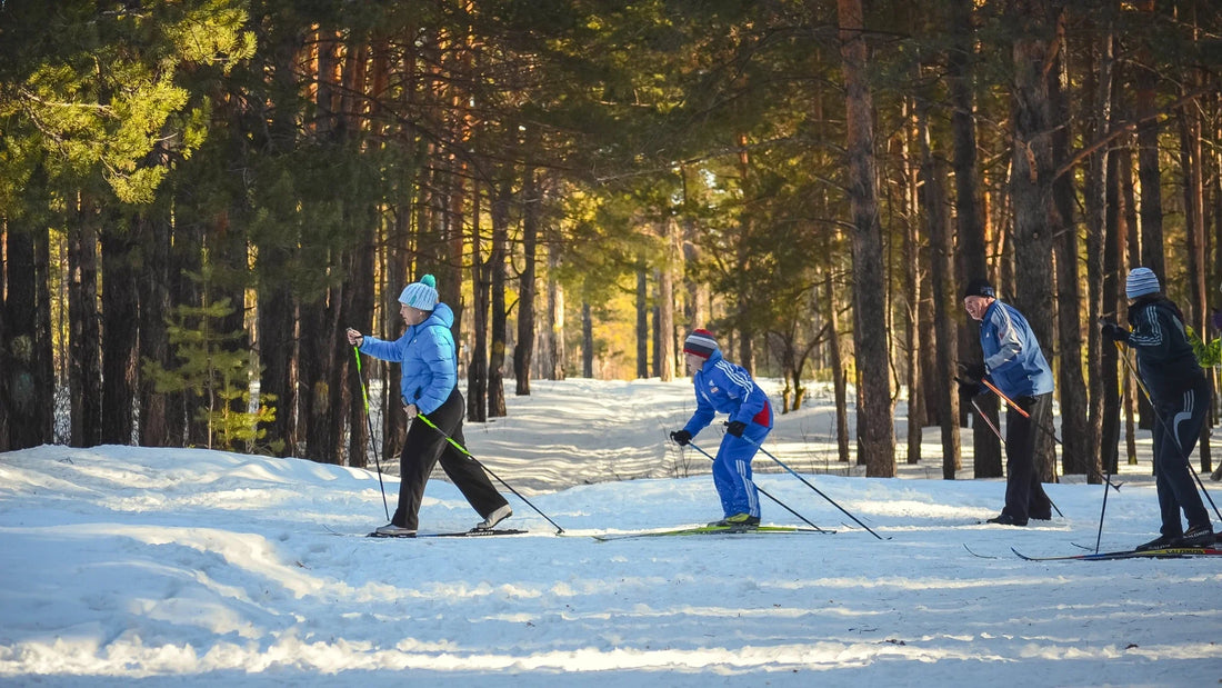 Group of senior skiers gliding through a sunlit forest trail in winter, showcasing the active lifestyle supported by Laetts ski socks with HygroHeat™ and BootGlide™ technologies