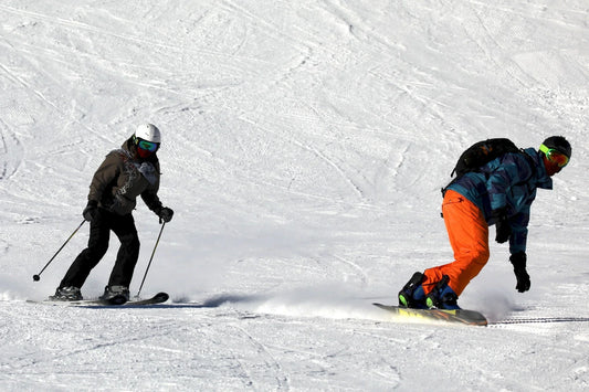 Skiers and snowboarders descending a snowy mountain slope, illustrating the contrast between skiing and snowboarding footwear performance.