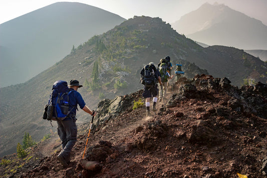 Hikers with backpacks trekking up a rocky ridge at sunrise, dust trailing behind—banner for Laetts HygroHeat™ Merino Thermal socks, highlighting FIR-powered warmth and moisture control for long hikes.