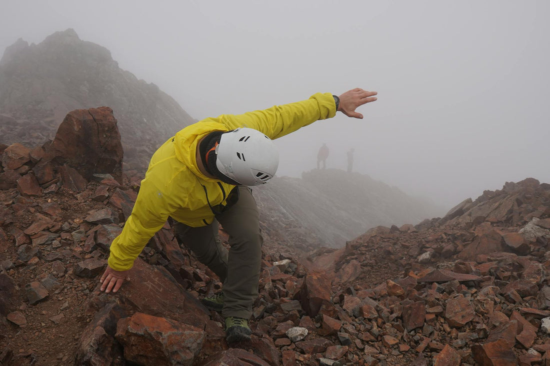 Hiker in a yellow jacket scrambling along a foggy, rocky ridge—banner for Laetts compression socks with HygroHeat™, highlighting graduated support and FIR-powered warmth for long hikes and rugged exploration.