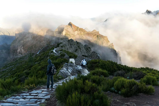 Hikers walking along a mountain ridge trail in changing weather conditions, illustrating variable environments and outdoor activity.