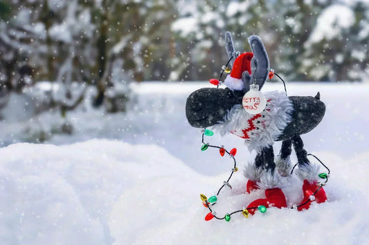 Festive winter scene with a plush reindeer wrapped in colorful Christmas lights standing in fresh snow.
