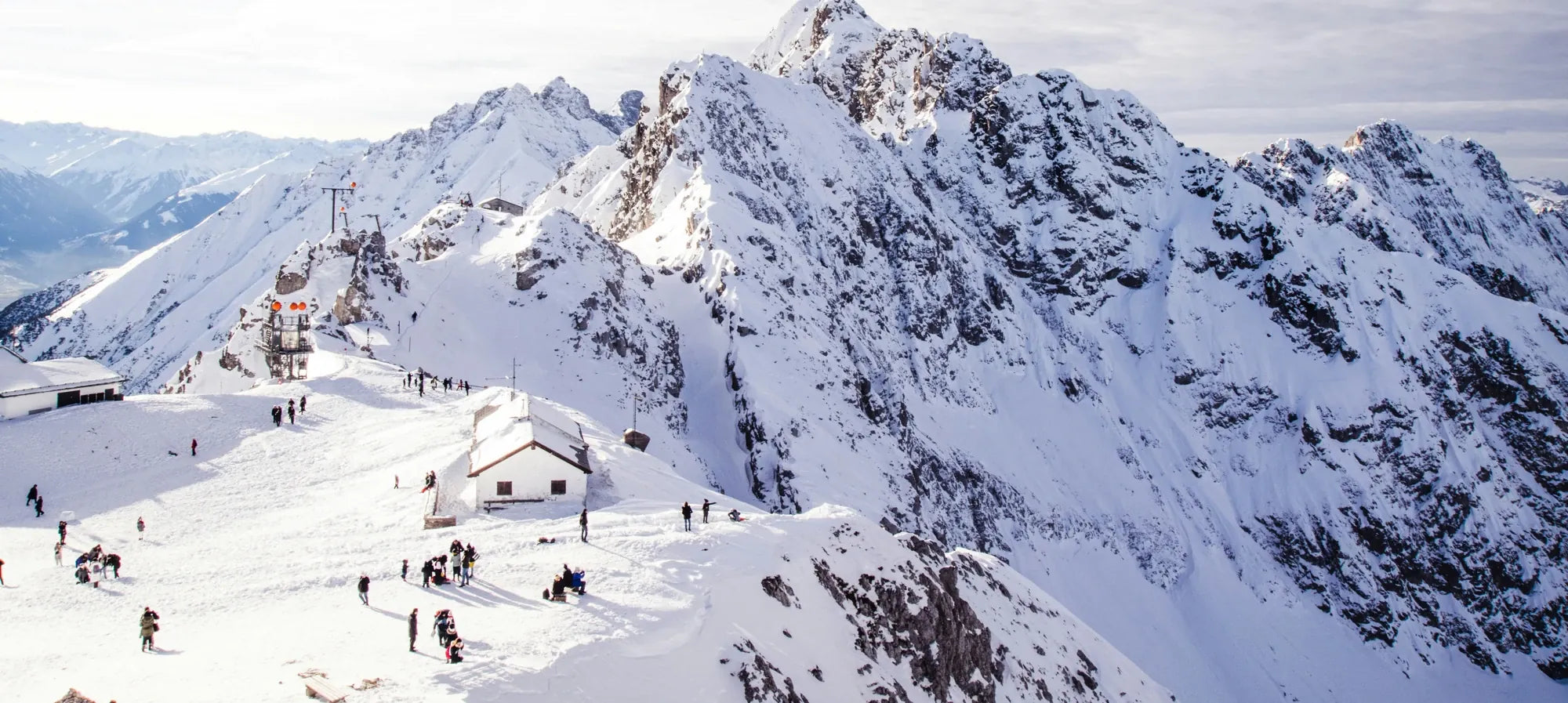 A snowy alpine mountain with skiers walking near a lodge, illustrating extreme cold conditions where Merino thermal socks provide warmth.