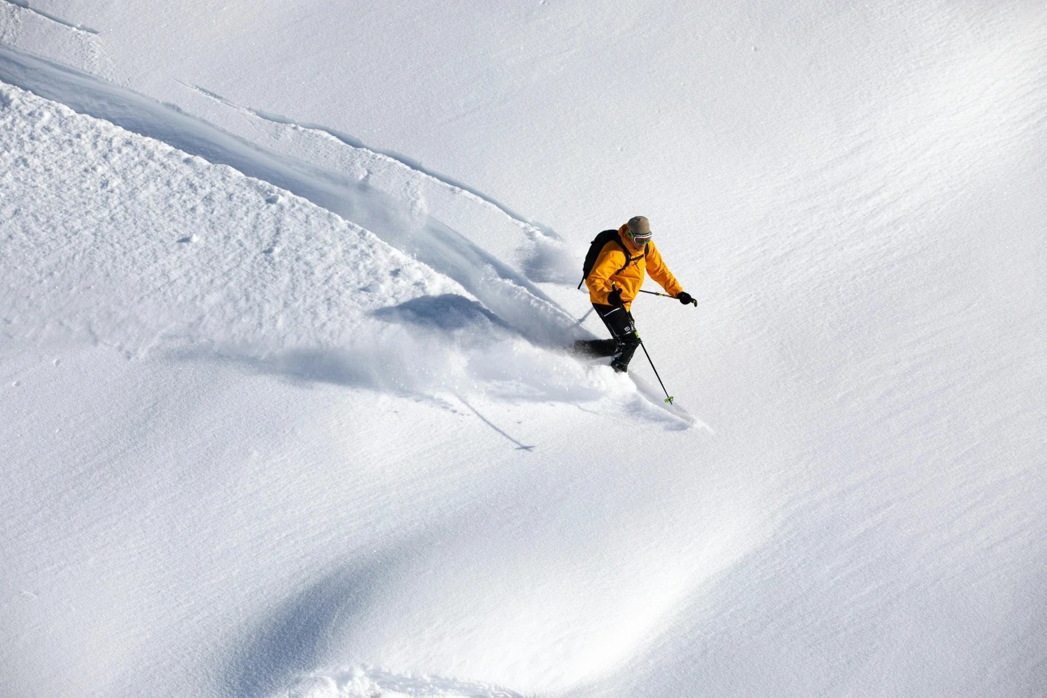 Skier carving through powder in bright yellow jacket on a mountain slope — represents Laetts BootGlide™ Luxury Collection of premium Merino ski socks with effortless boot entry and advanced performance.